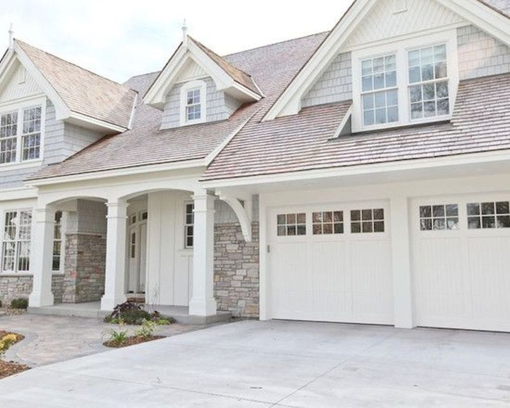 Farmhouse exterior design with white gable accents, white columns and covered porch, light colored natural stone, coordinating light colored shake roof