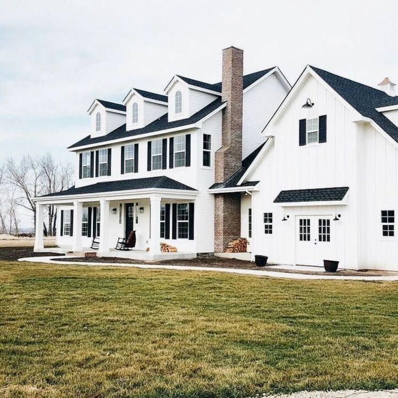 Modern farmhouse exterior design with dark room, white walls, plank siding, white windows & trim, black shutters, brown stone, chimney, covered front porch
