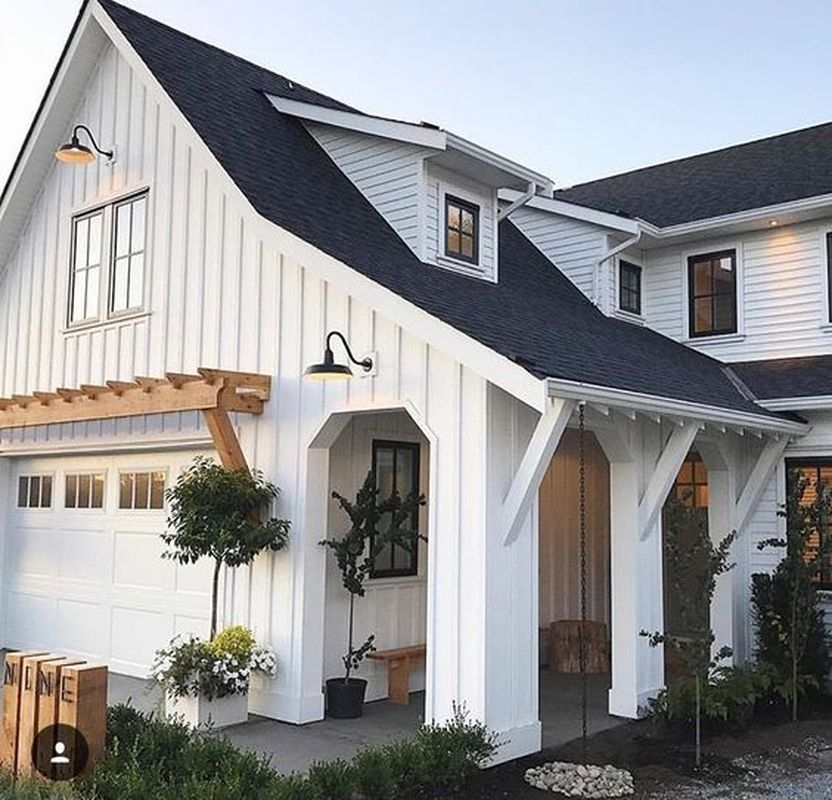 New construction modern farmhouse for exterior design with white plank siding, dark roof, covered porch with columns, extra overhang & angled beams, natural wood trellis above garage door