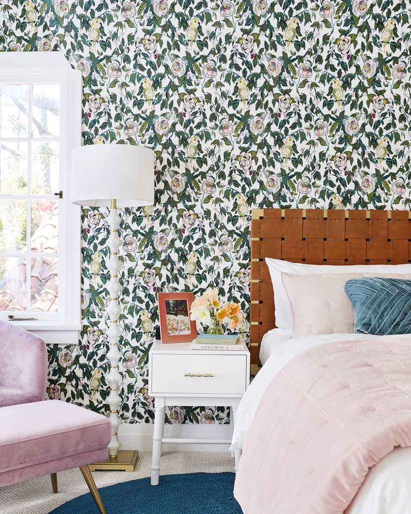 A cozy bedroom design with flower wallpaper, a white window, a white night stand to store house plant, and floor lamp to create good lighting