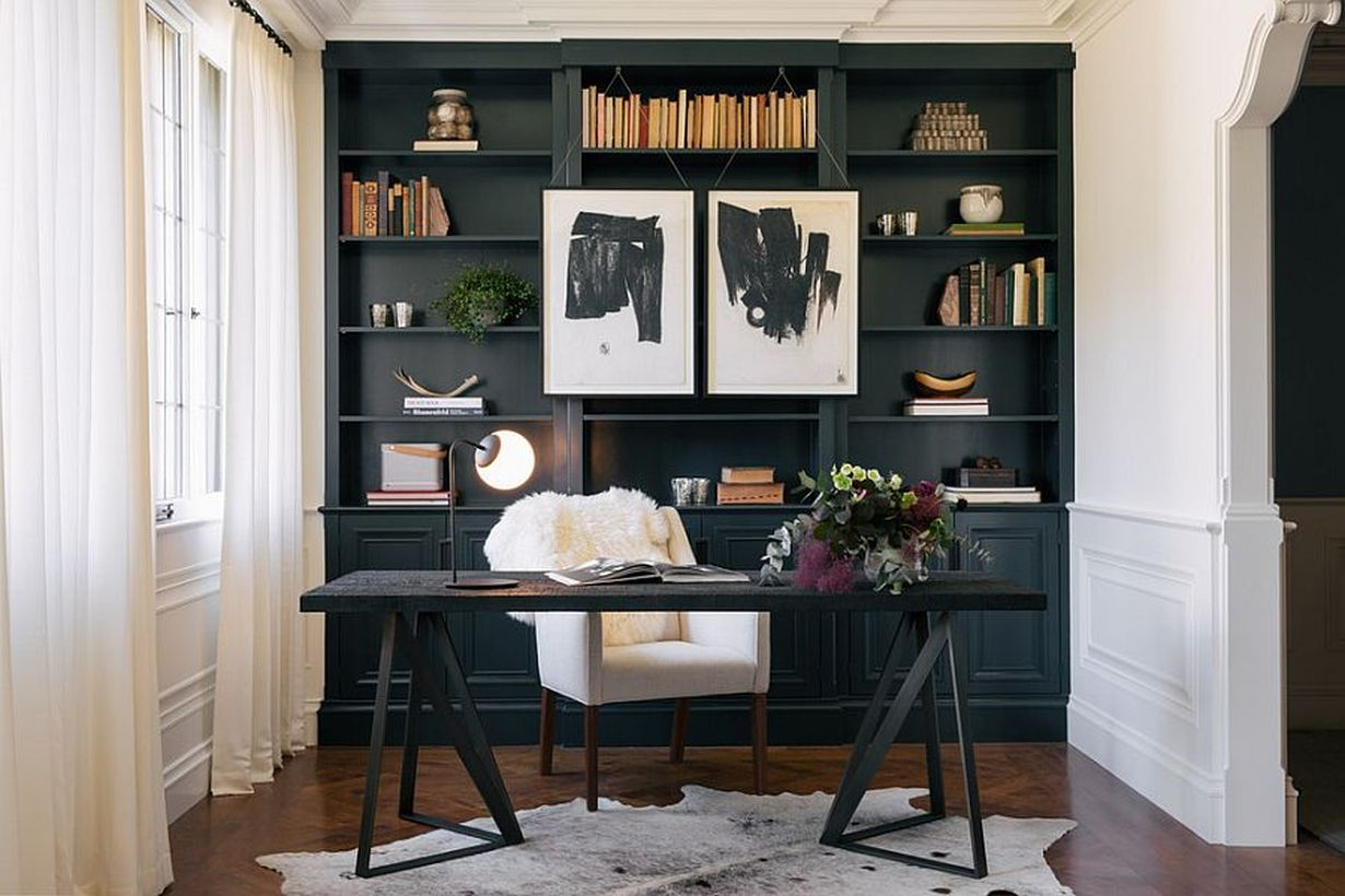 A minimalist black and white home office with white walls, a large black bookshelf, white curtains, painting hung on the bookshelf, black wooden table in the small space