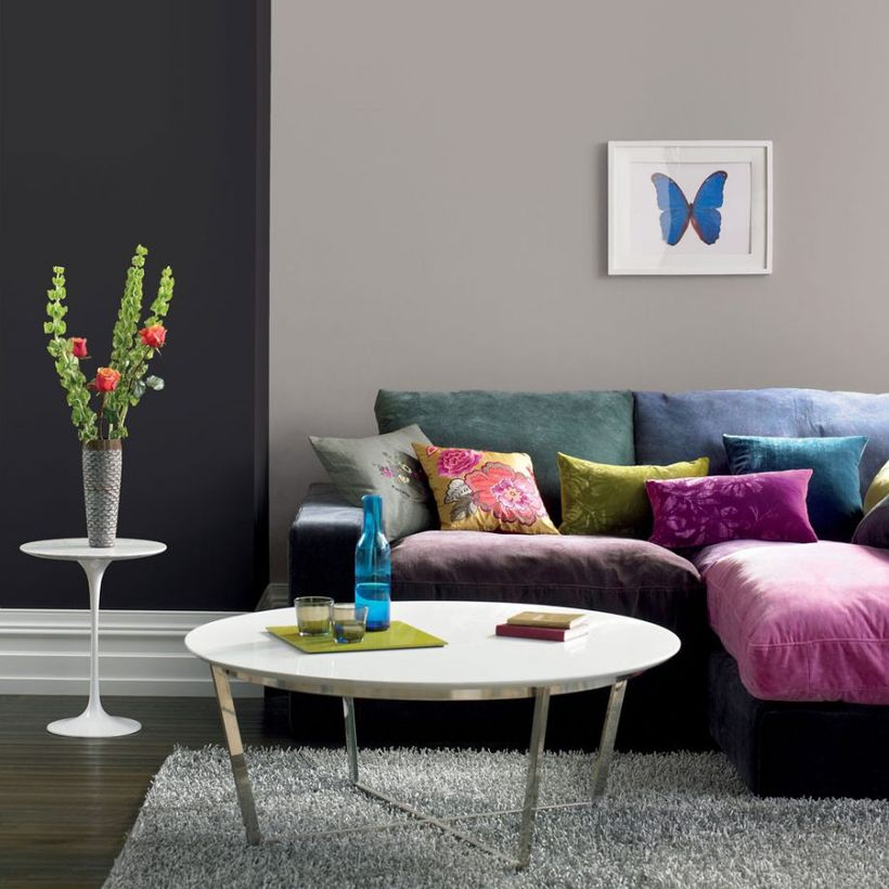 A simple living room grey home design with black and grey walls, soft sofas colorful, a round white coffee table, a white table to put some house plant, and a soft gray carpet