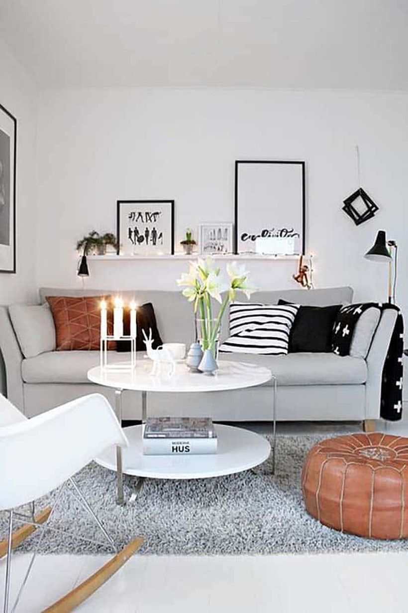 A simple monochrome living room design with white walls, a grey sofas, a white round coffee table, a long hanging rack to place artworks, adn decorative lighting to create good lighting