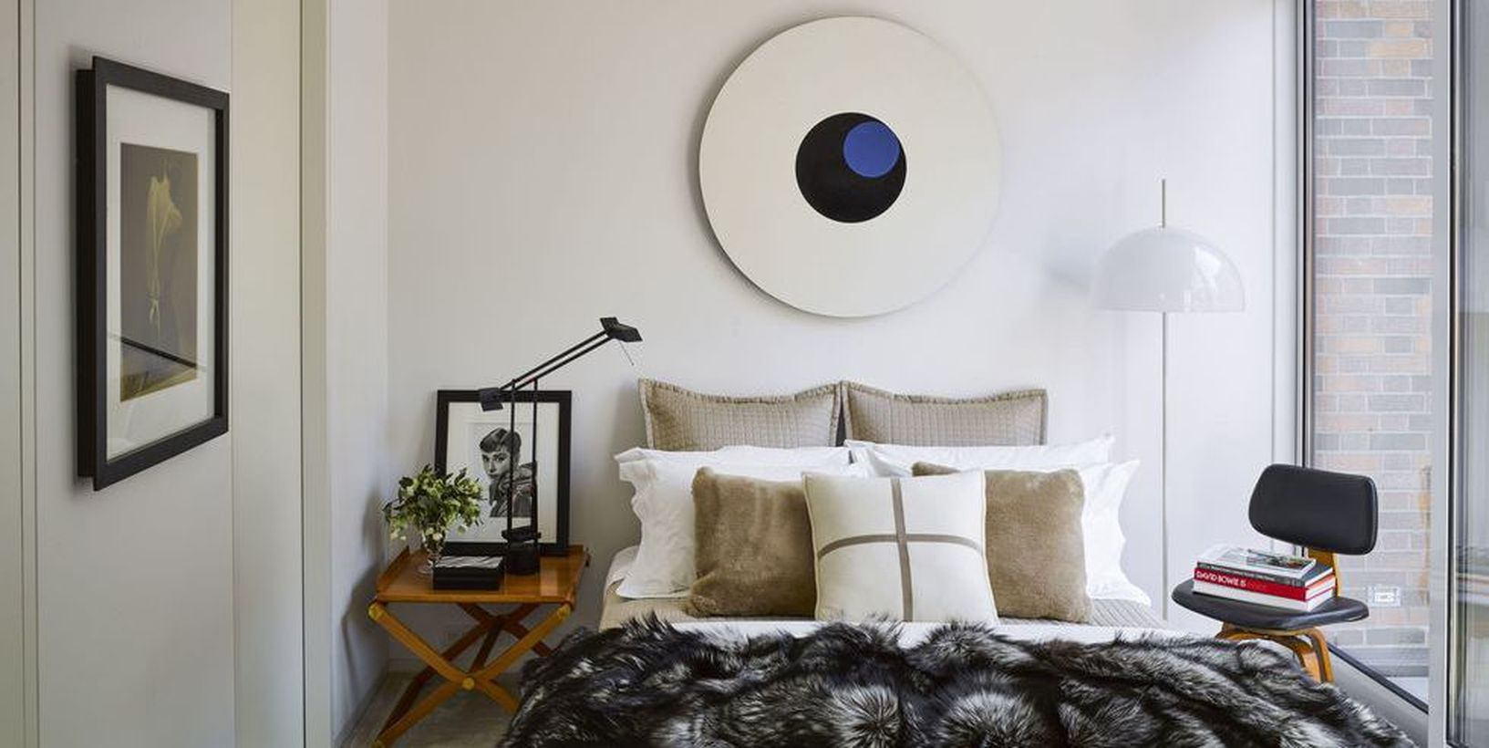 An elegant guest bedroom appeals with nightstand on beside to store gallery, rounded shapes in the lamp and artwork in the small space