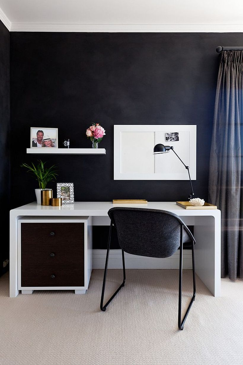 An elegant home office with a white hanging rack on the black walls, a white table, and table lamp