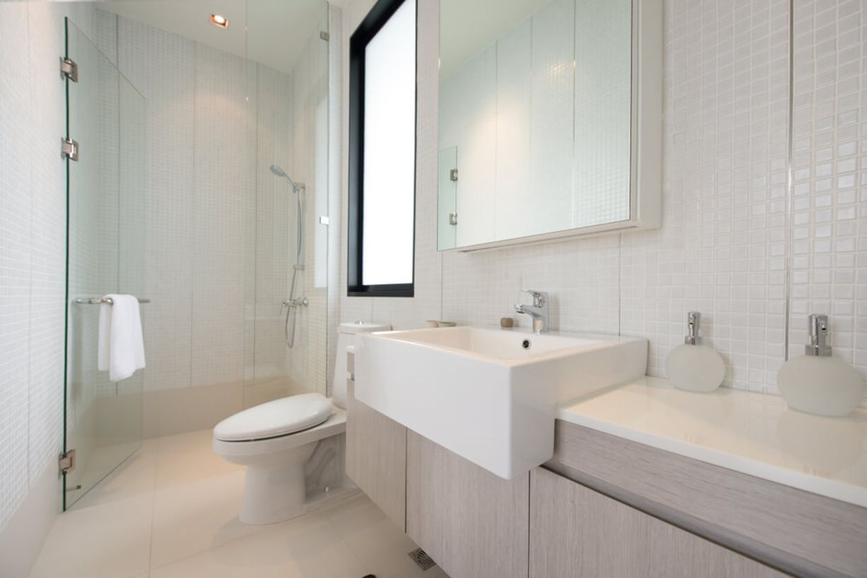 An elegant white bathroom decor ideas with white plaid ceramic walls, a white sink, a towel hook on the glass door, and grey bathroom storage cabinets