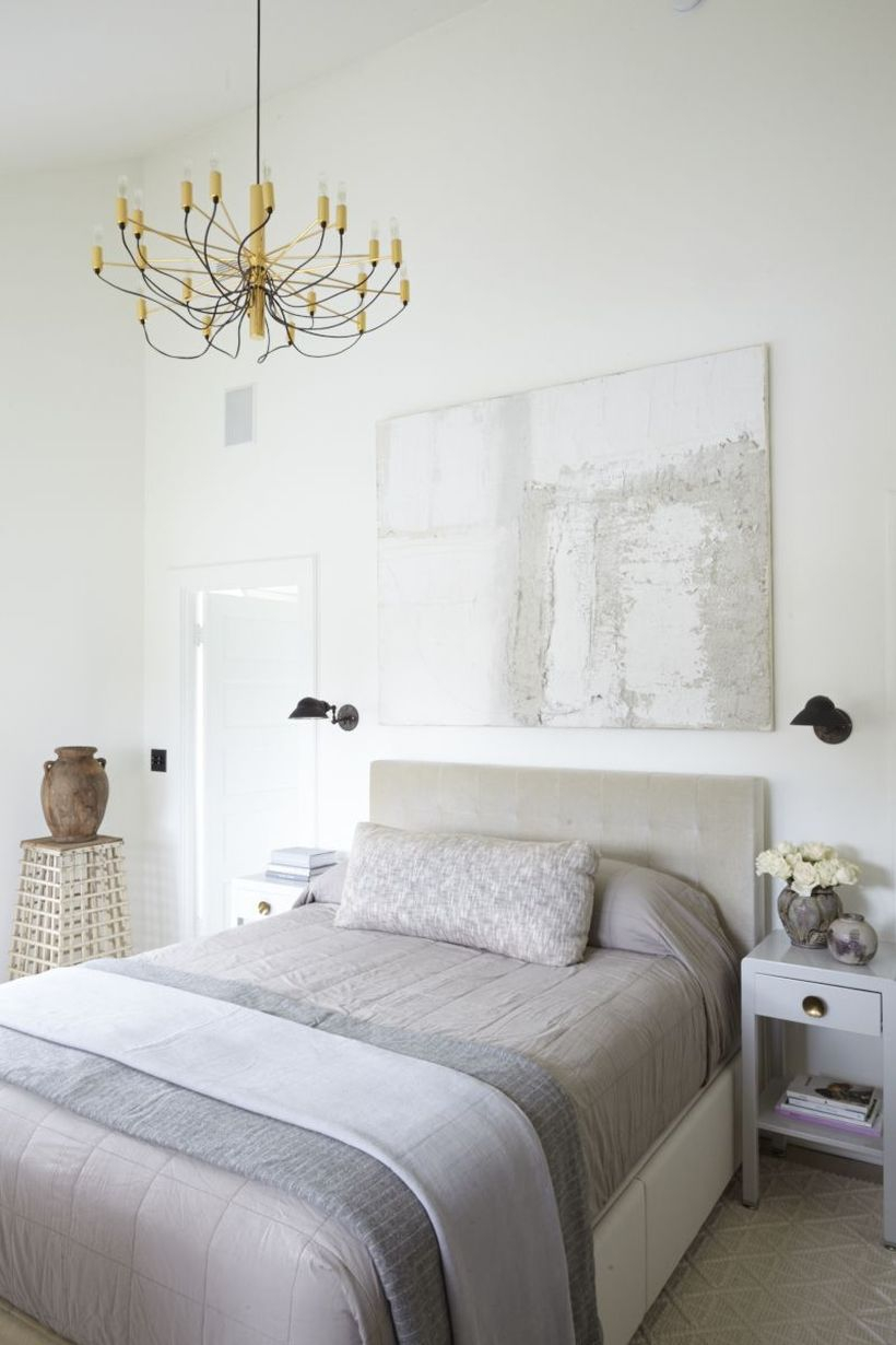 The minimalist bedroom with neutral palette, modern art on the walls, a vintage nightstands and a statement chandelier to create good lighting