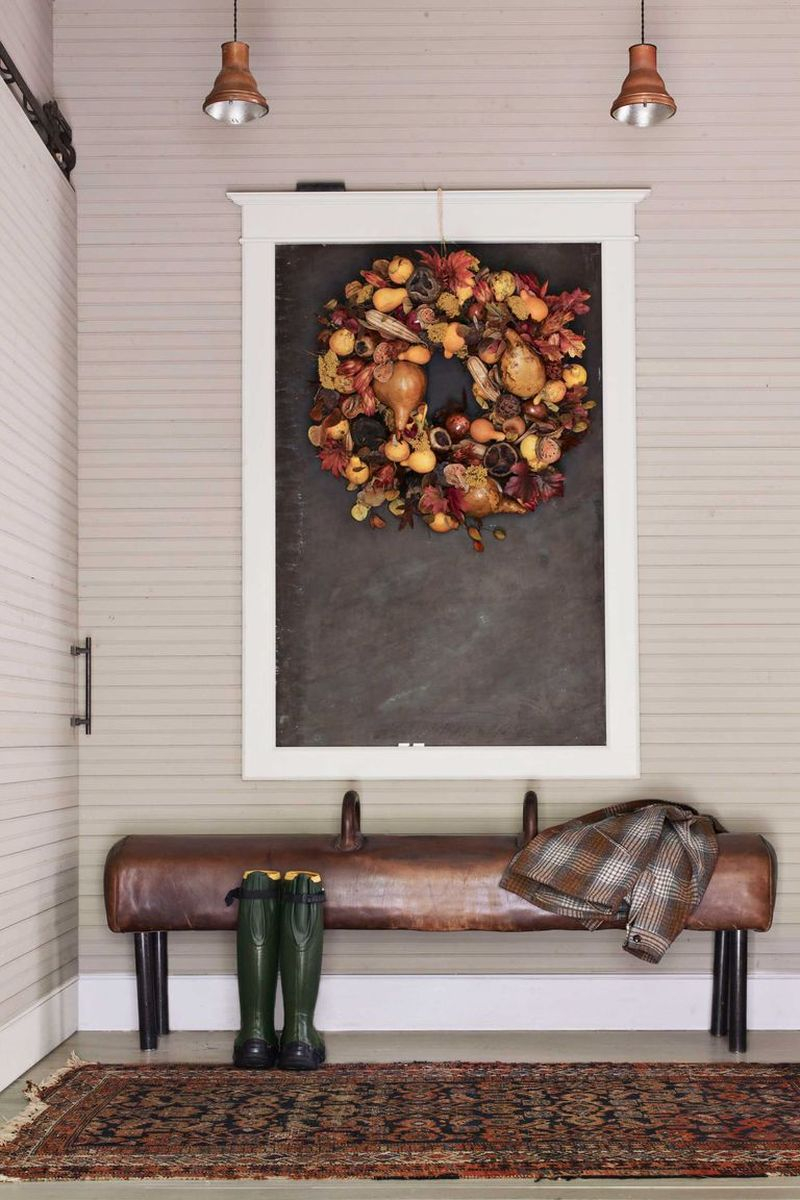 A gymnastics pommel horse with its legs shortened, serves as a bench in a entryways and the seasonal wreath hangs on a framed chalkboard