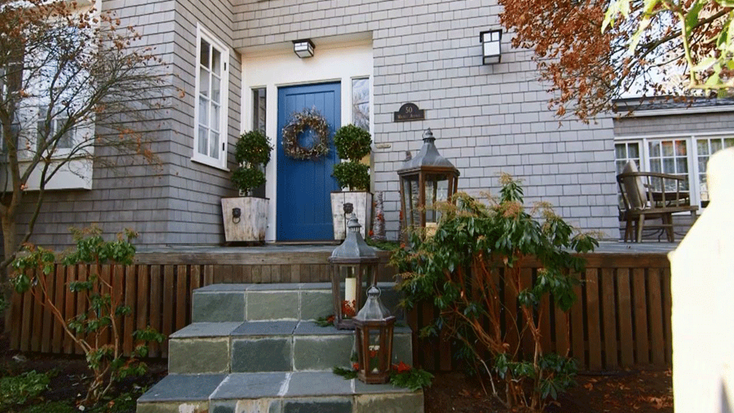 An adorable farmhouse porch ornament with plants in pot square, candle lights, lights on walls and wreaths