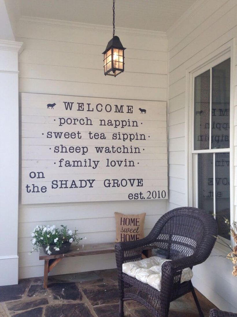Simple farmhouse porch ornament with a plant above on wooden chairs, a black hanging lamp, and white paintings from wood