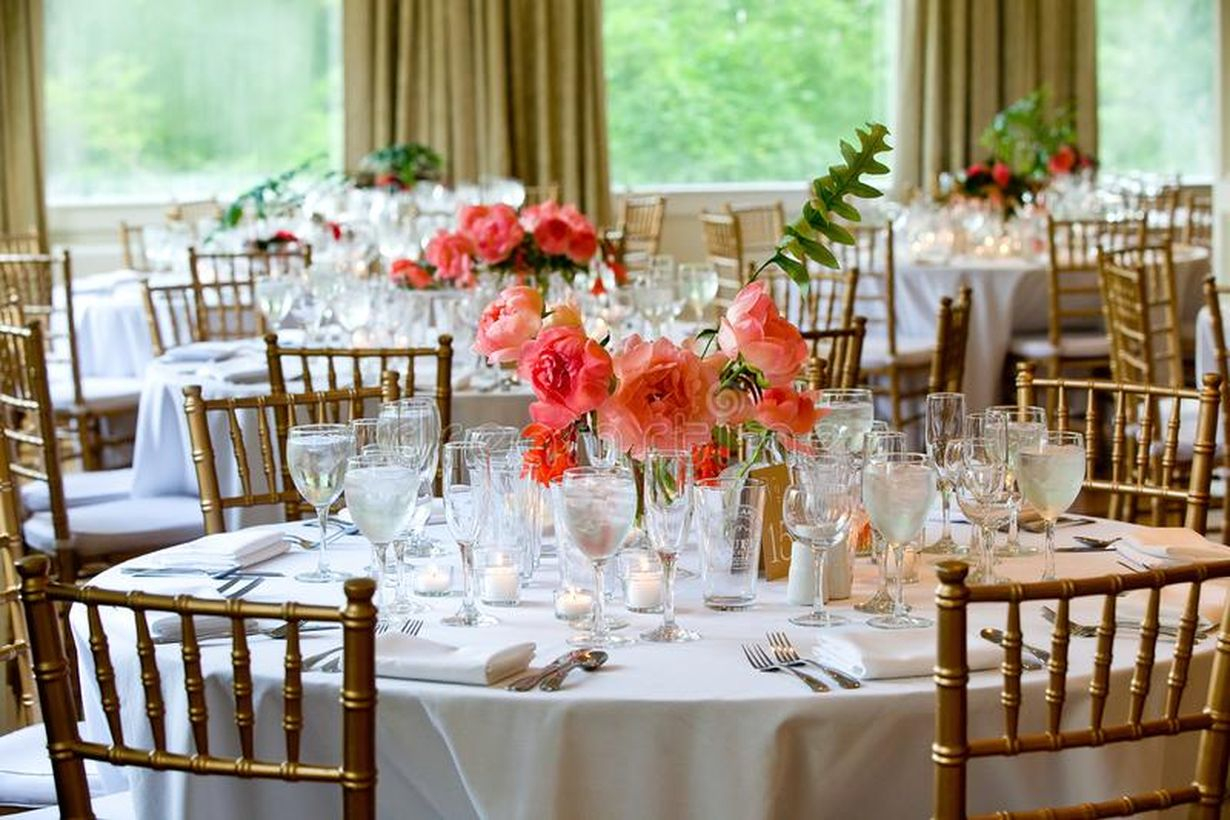 A beautiful indoor table set for wedding with white tables set for beautiful indoor catered luxury wedding event with flower arrangements.