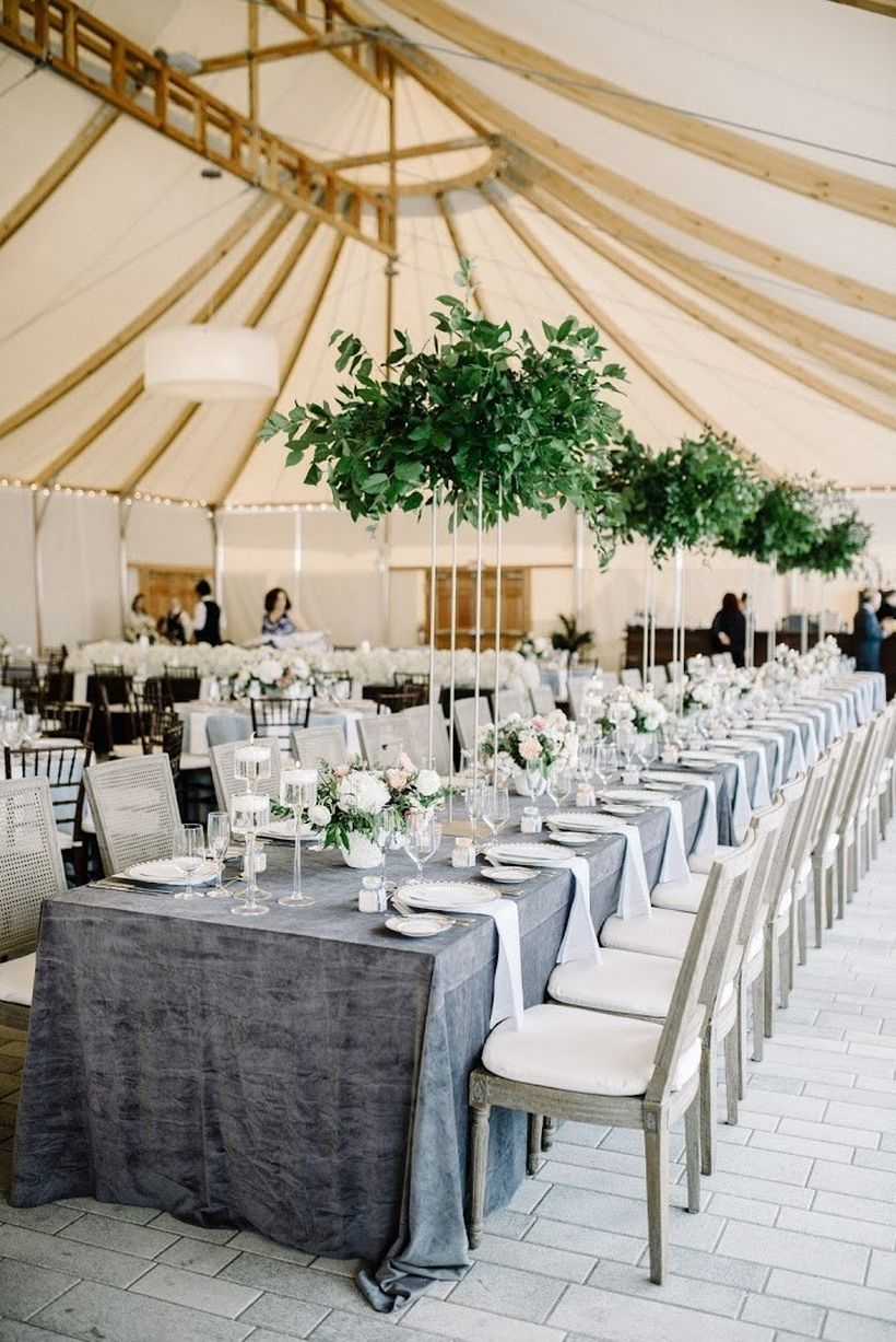 A creative indoor table set for wedding with long wooden table classic, gray tablecloth, greenery, chandeliers are a fairly inexpensive way to make an impact at your reception.
