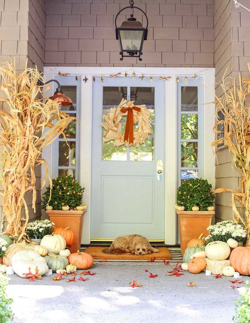 An awesome outdoor redecoration from summer to fall with beautiful matching corn stalks, an array of pastel pumpkins, mini pumpkin and a charming door