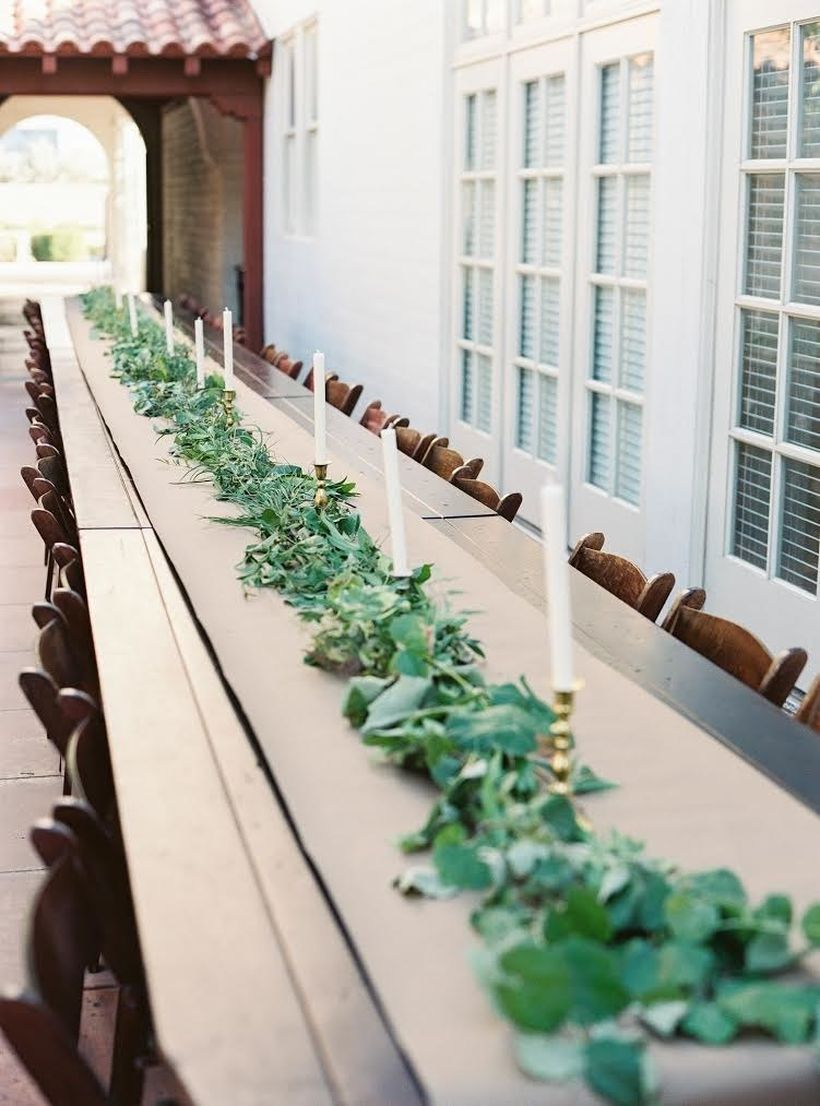 An elegant outdoor table set for wedding with wooden tables, craft paper, a garland made only of greenery and candlesticks to round out this classic look.