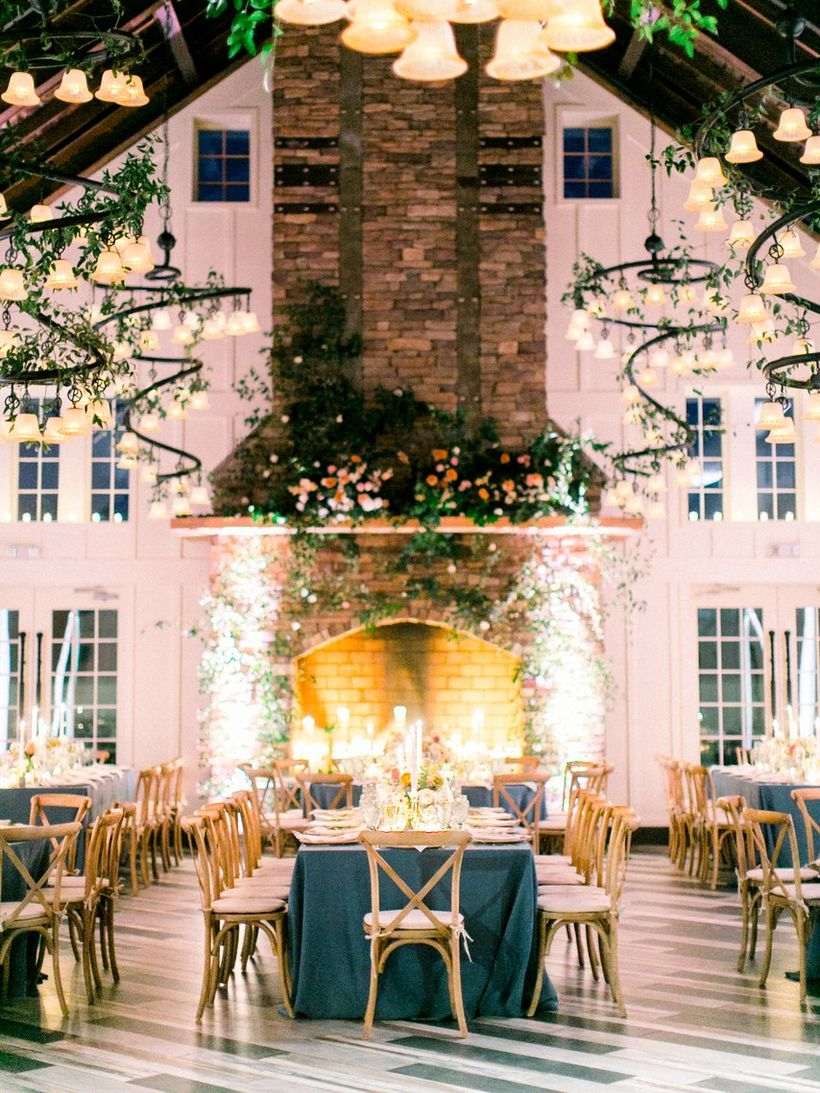 An exciting indoor table set for wedding with wooden tables dark blue linen in a huge and open room like this it adds some drama.