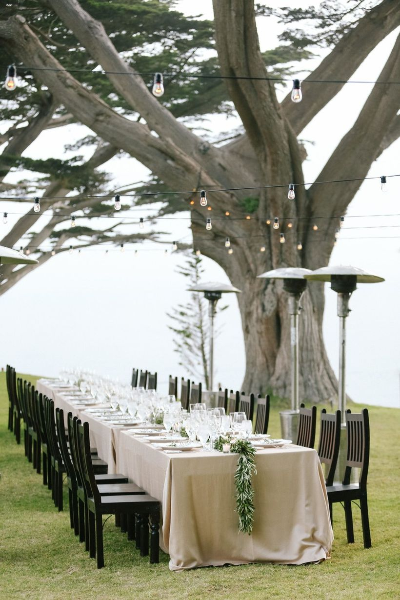 An extraordinary outdoor table set for wedding with long elegant table, crisp dinnerware, ps heat lamps and lined, dark wooden chairs.