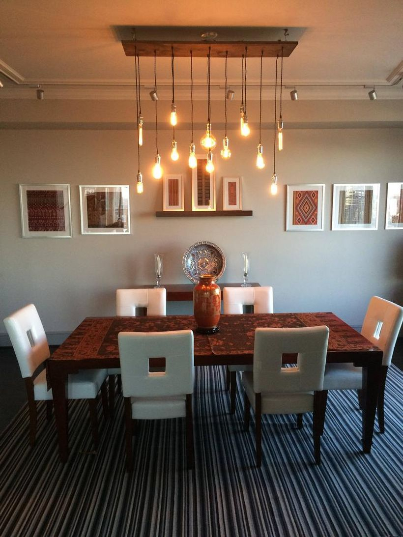 A creative rustic chandelier for dining room with 14 pendant wood chandelier, black table, white chairs, large carpet and decoration on the wall.