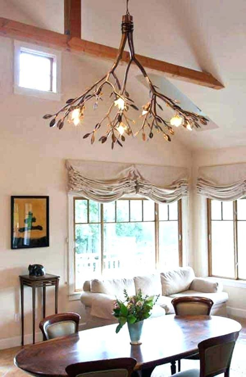 A magnificent rustic chandelier for living room with tree branch chandelier, white sofa, wooden table, wooden chairs, big window and flower vase.