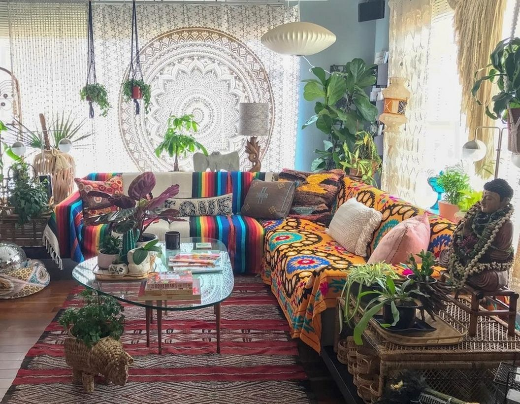 An amazing boho living room with colorful sofa, patterned red carpet, combined with white patterned curtains, green plants in the corner and plants in small pots on rattan tables