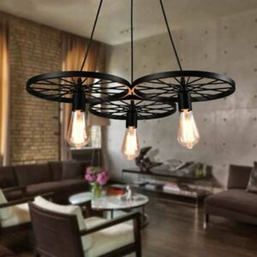 An adorable rustic chandelier for living room with 3 black wagon wheel chandelier, brown sofas, white chairs, wooden floor, brick stone wall and round white table.