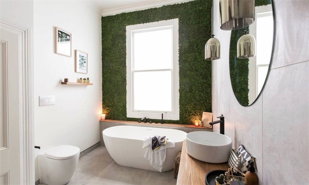 An amazing bathroom design with round mirror and white tub combined with moss near the window to beautify your bathroom design