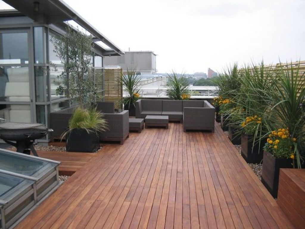 An awesome rooftop design with dark sofa combined with wooden floor and plants around it to perfect your rooftop garden