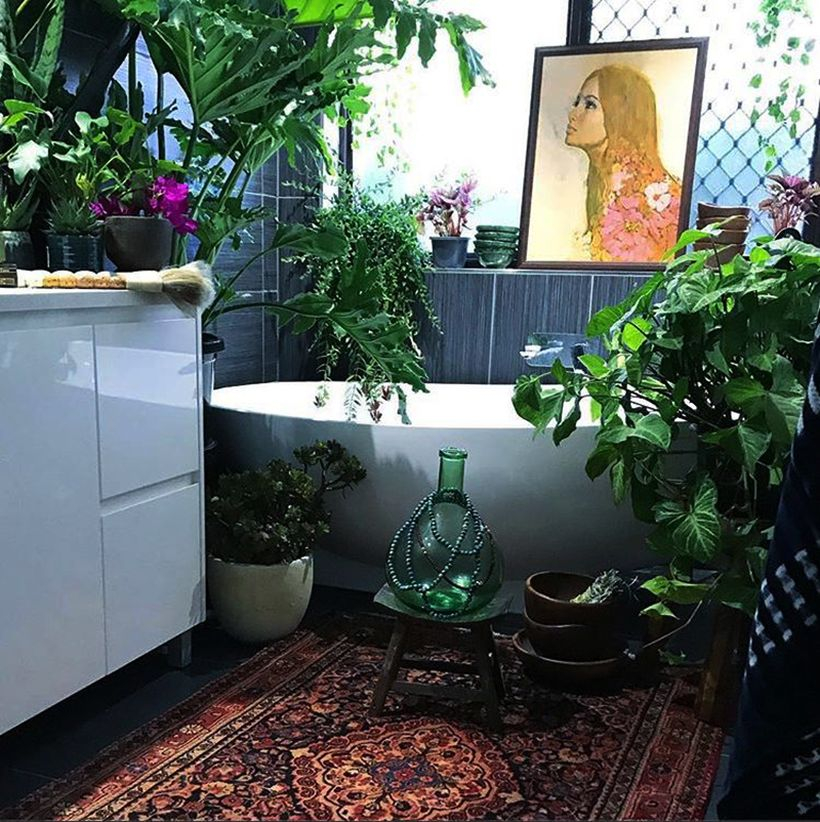 Gorgeous boho bathroom decor with square carpet motif, white storage cabinet, painting on the edge of the bathtub and green cover for air conditioning