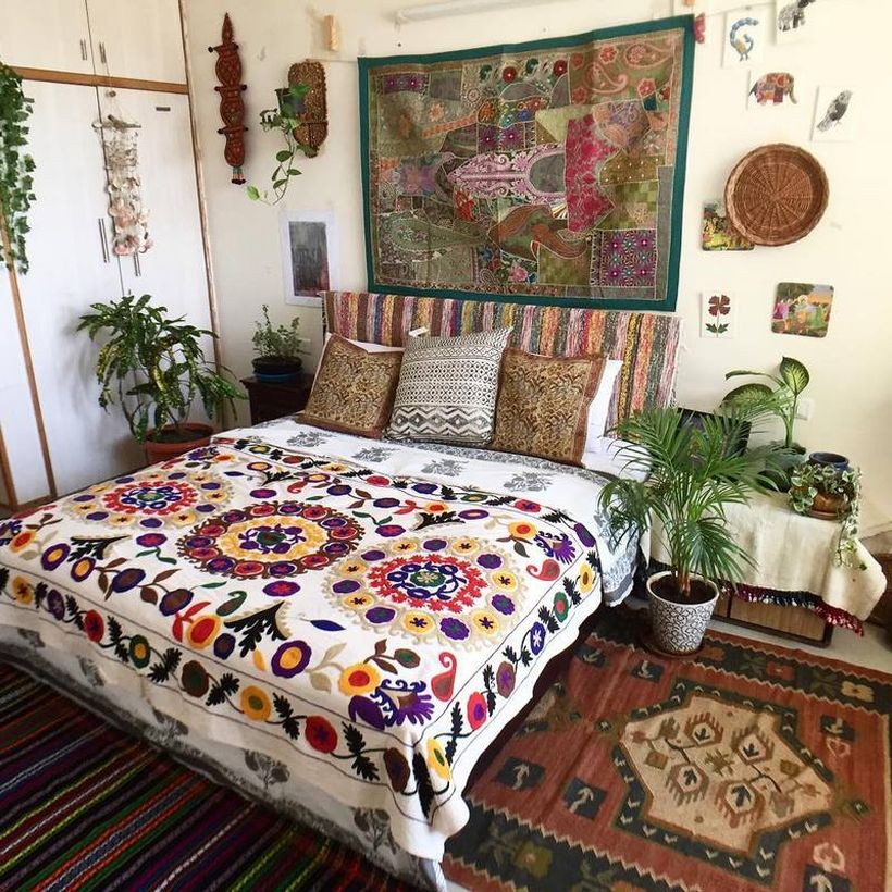 Interesting boho bedroom style with colorful floral motifs on white blankets, patterned pillows, classic wall art fabric tan green plants to complement the decoration