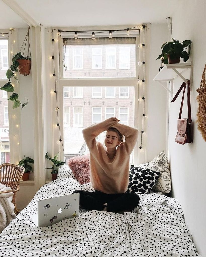 Interesting girls room decor with mattress and blanket motifs with black spots, colorful pillows, hanging plants, plants on white shelves and decorative string lamps