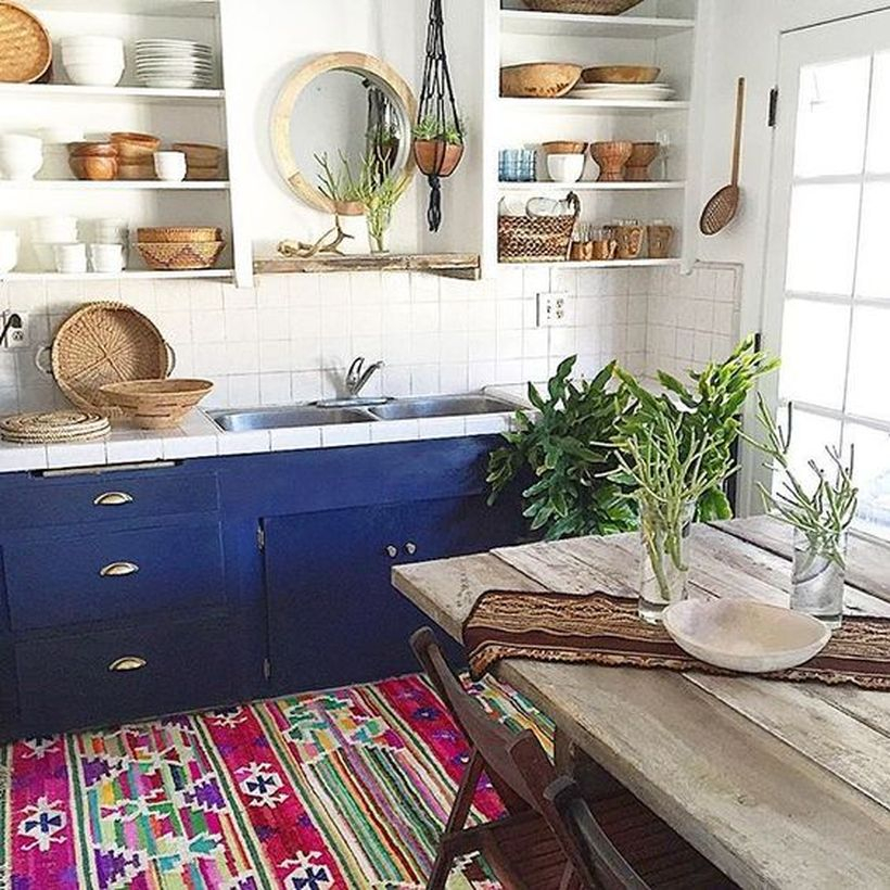 Colorful boho kitchen flooring with blue cabinet, white storage rack, wooden table and plants