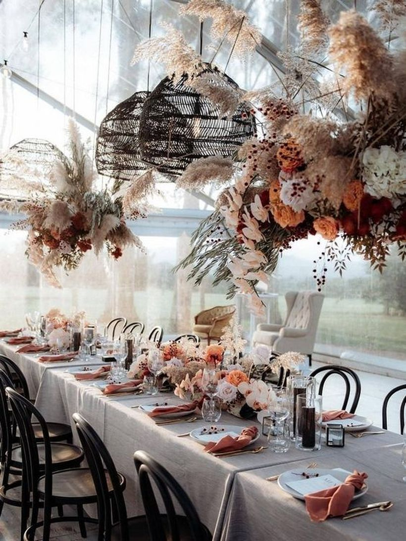Boho chic table in rust and blush shades with lush florals on the table and over it, wicker lamps, colored napkins and candles