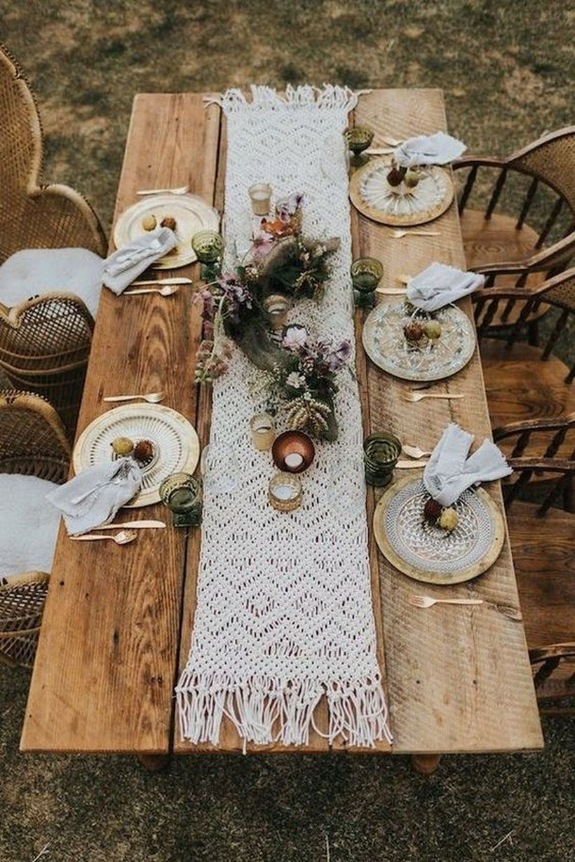 Boho chic wedding table setting with a macrame table runner, dyed napkins, lush florals and greenery, gilded plates and candles