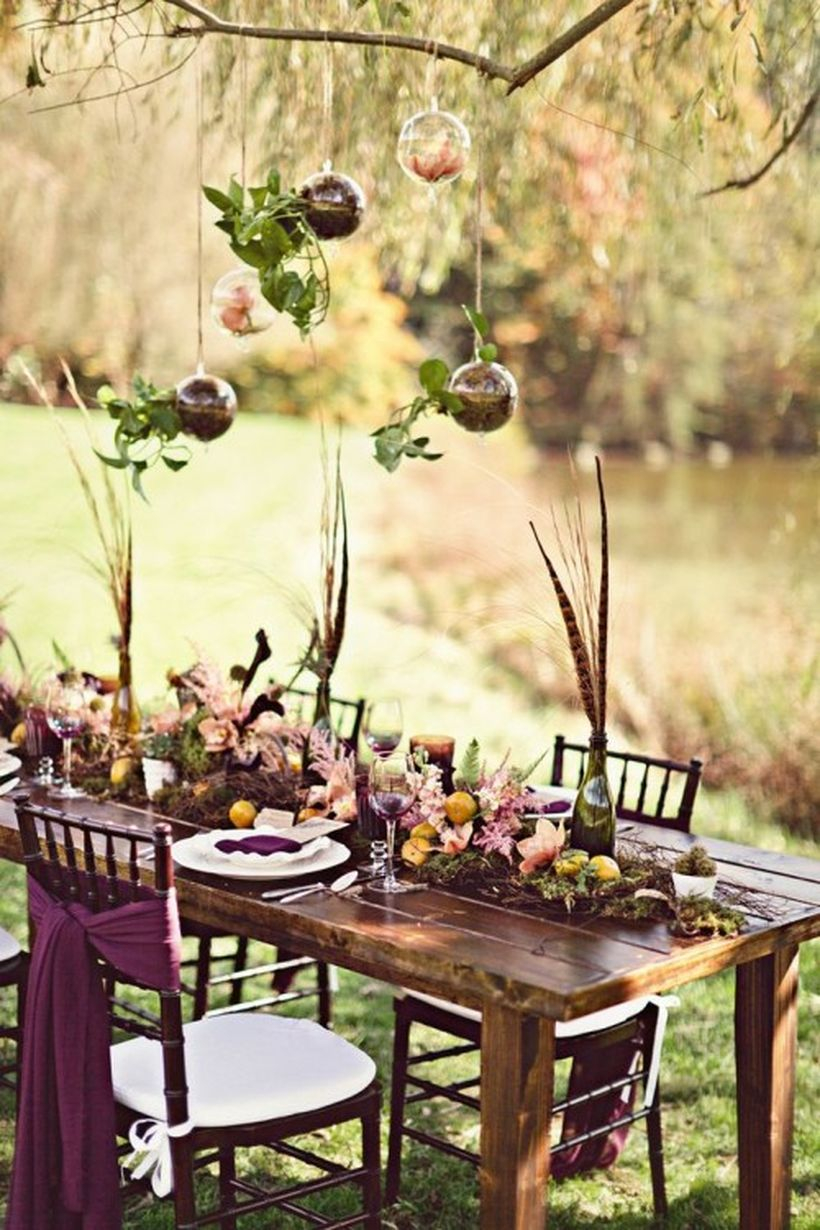 Boho tablescape with a moss and bloom runner, feathers in bottles, colorful textiles and suspended ornaments with petals