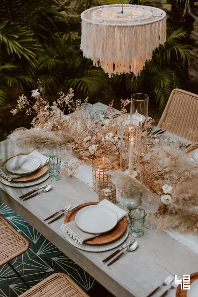 Boho tablescape with wooden plates, a fringe chandelier, candles, dried herbs and blooms plus pampas grass