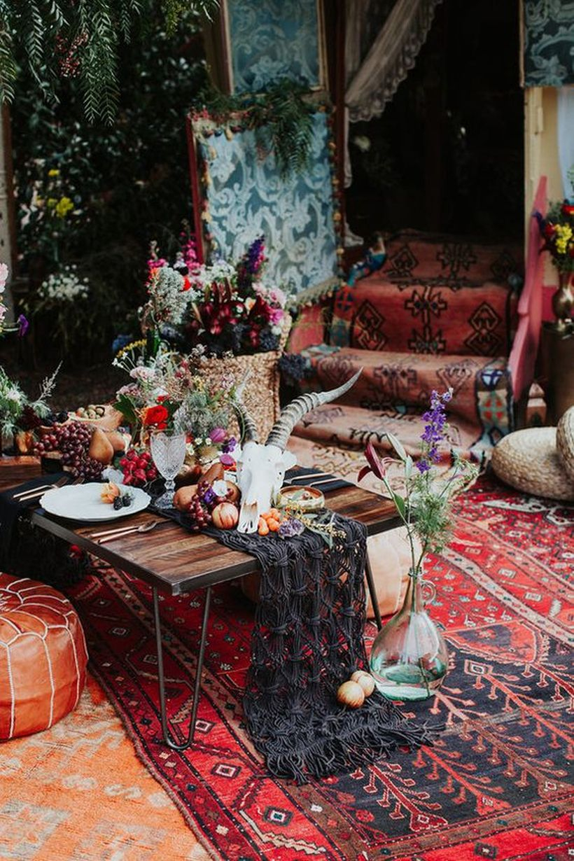 Picnic tablescape with a black macrame runner, an animal skull, fruits and veggies on top plus greenery