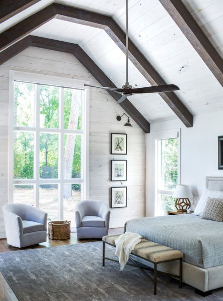 A-large-airy-farmhouse-bedroom-done-with-white-walls-dark-stained-ceiling-beams.-1