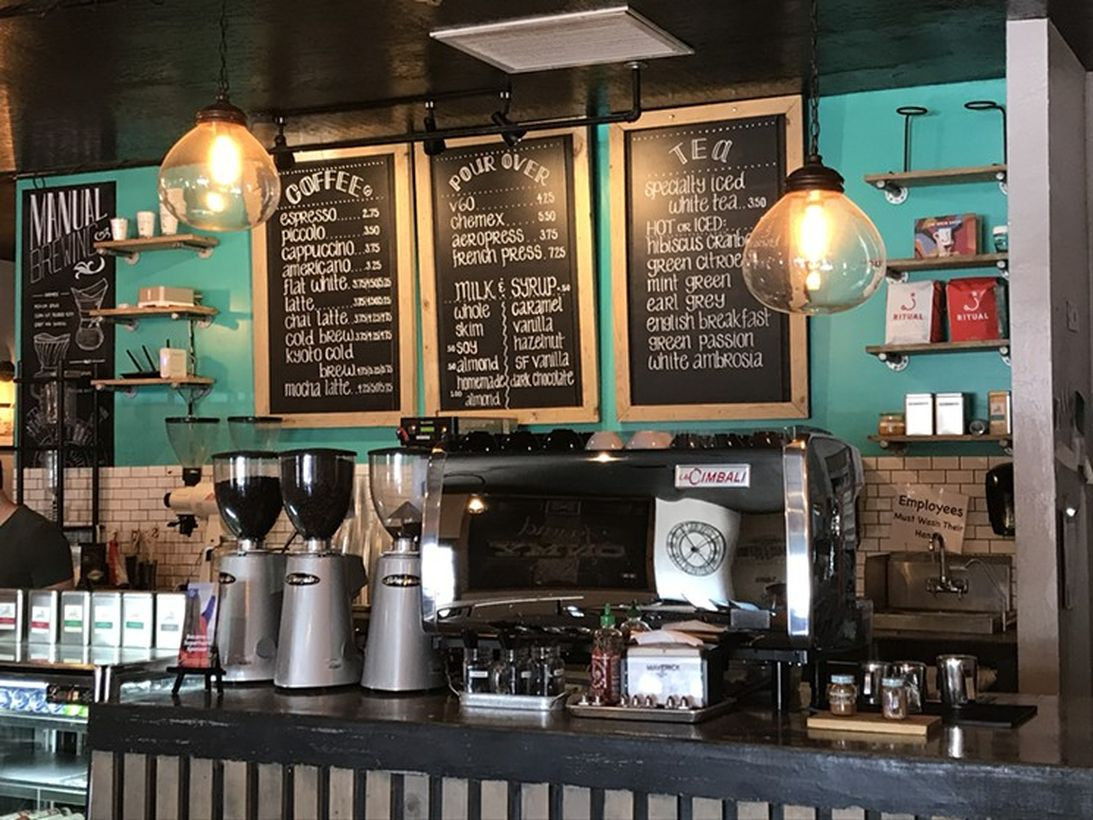 Dark brown wooden coffee bar with chalkboard, green wall and hanging lamps