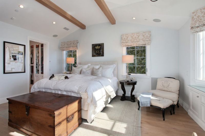 Farmhouse-bedroom-with-light-colored-walls-wooden-beams-floral-curtains.-1