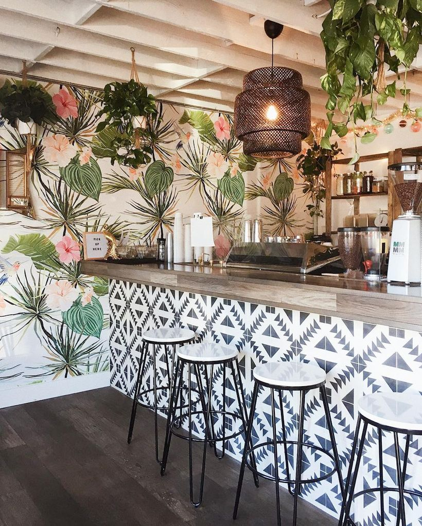 The decor of white patterned black coffee bars combined with unique chandeliers, green hanging plants, plant motifs within the white walls and small white korsi