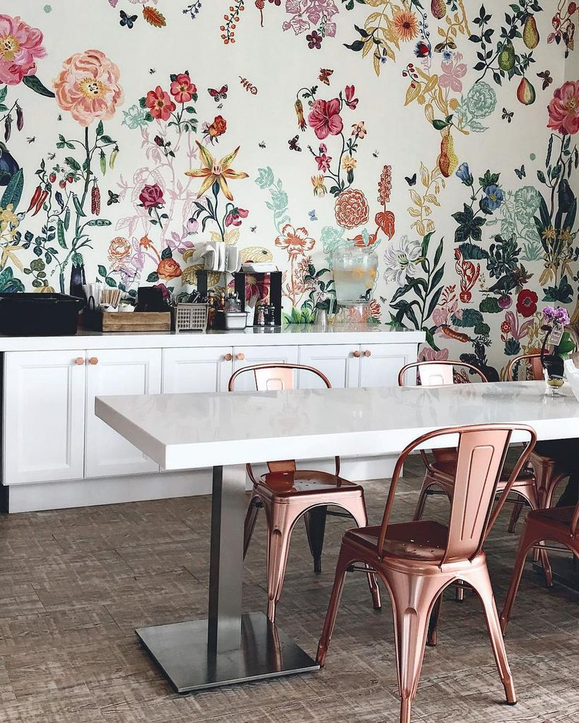 White coffee bar is combined with white plastic chairs and colorful floral designs inside the white walls
