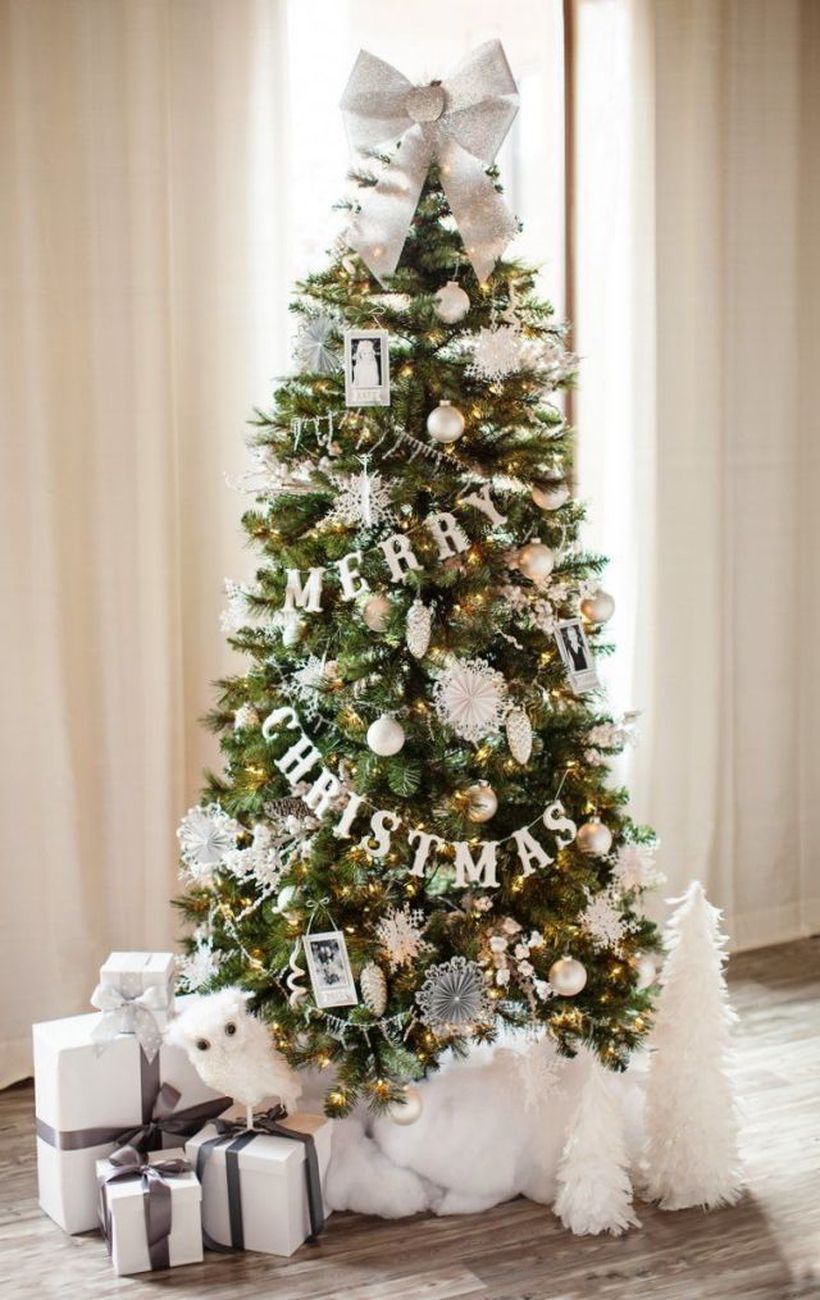 Small-green-christmas-tree-with-pine-ornaments-snow-ornament-and-large-ribbon-at-the-top-to-beautify-the-tree-decorations