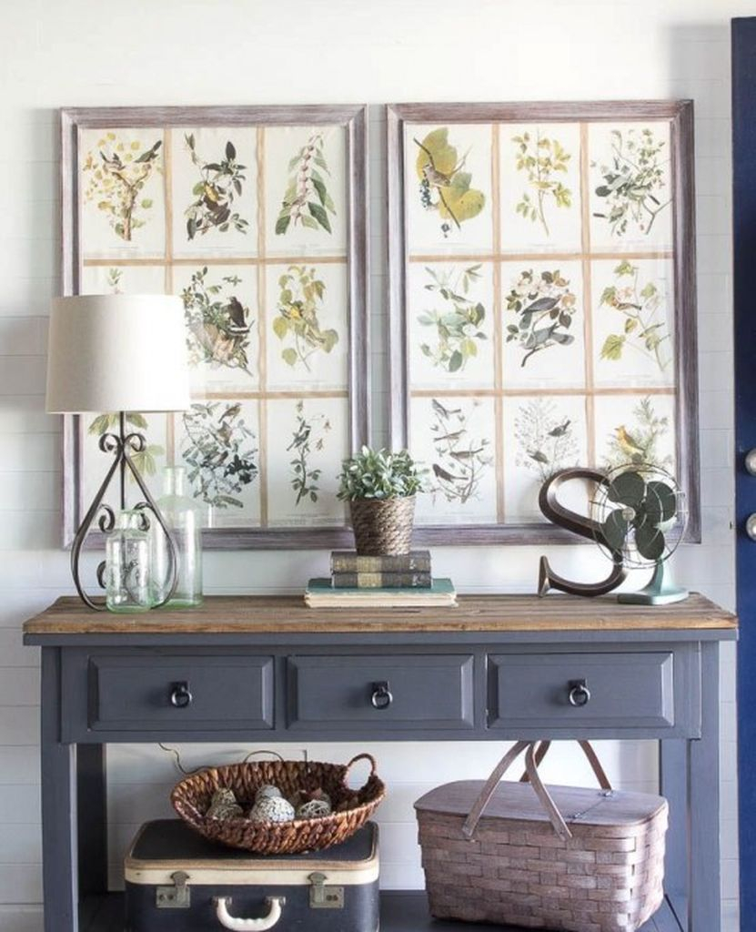 A grey console table with a stained tabletop, vintage posters as artworks, baskets and a potted plant for a cozy farmhouse entryway