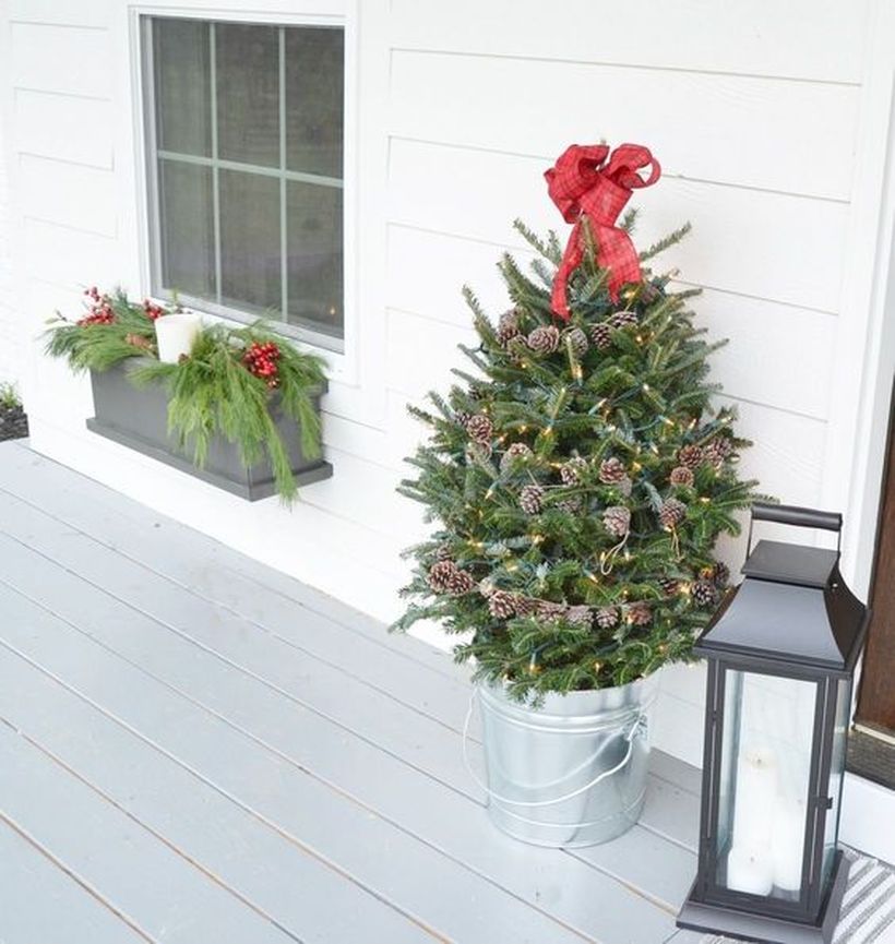 22-a-small-holiday-tree-decorated-with-lights-pinecones-and-a-red-bow-on-top-in-a-galvanized-bucket-for-a-porch