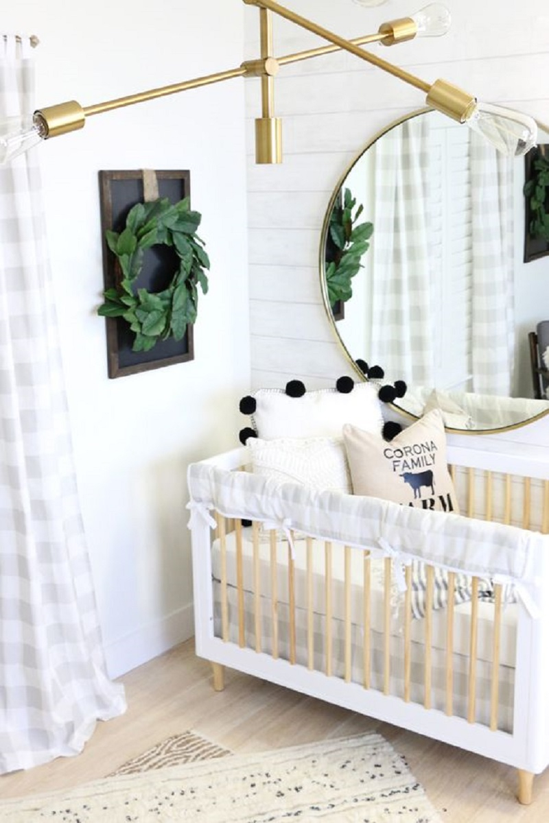 A-modern-farmhouse-nursery-with-white-plank-walls-a-neutral-wooden-crib-a-gold-chandelier-and-a-greenery-wreath