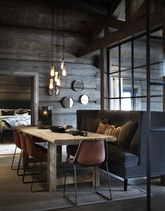 A-moody-chalet-dining-space-with-a-large-black-sofa-pendant-bulbs-a-wooden-table-and-leather-chairs-1