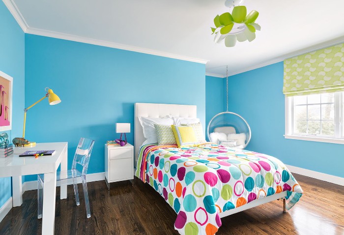 Blue-walls-and-a-white-ceiling-in-a-room-with-dark-brown-laminate-floor-and-a-bed-with-a-colorful-duvet-teenage-girl-room-ideas-white-desk-and-a-clear-plastic-chair
