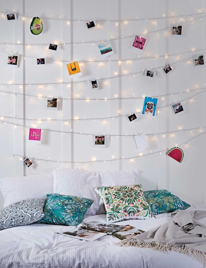 Eight-rows-of-lit-fairy-lights-decorated-with-photos-and-colorful-images-hung-on-a-white-wall-cheap-ways-to-decorate-a-teenage-girls-bedroom