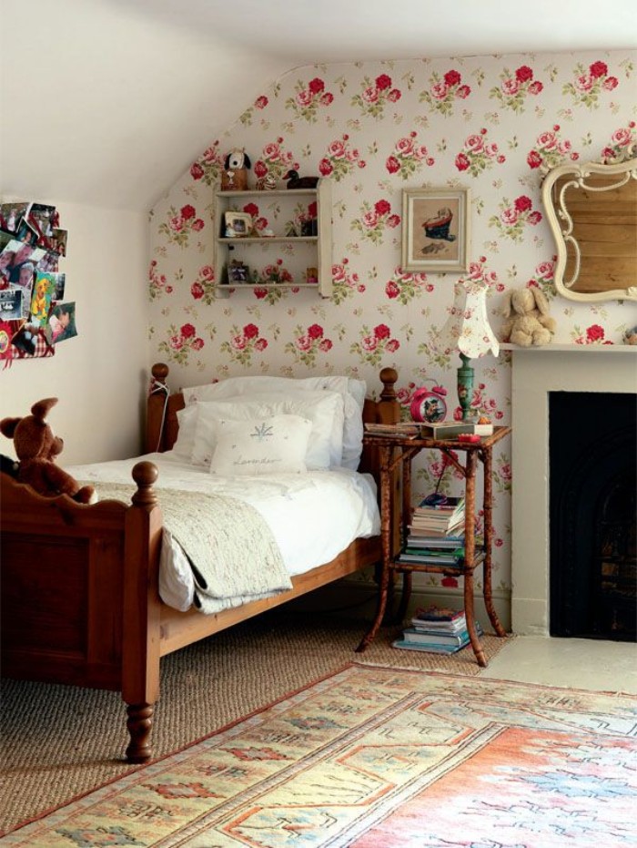 Vintage-style-wooden-bed-with-white-duvet-and-pillows-in-a-room-with-an-ornamental-rug-and-a-fireplace-teenage-girl-room-ideas-floral-wallpaper-on-one-wall