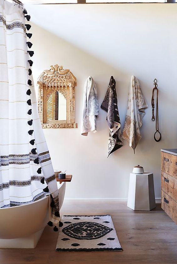 A-neutral-bathroom-with-a-boho-rug-a-curtain-with-tassels-printed-towels-and-an-ornate-mirror