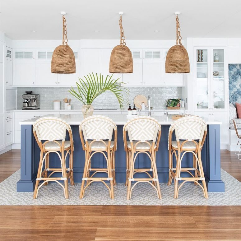 A-beach-kitchen-with-white-cabinetry-a-navy-kitchen-island-rattan-chairs-woven-lamps-and-greenery-775x775-1